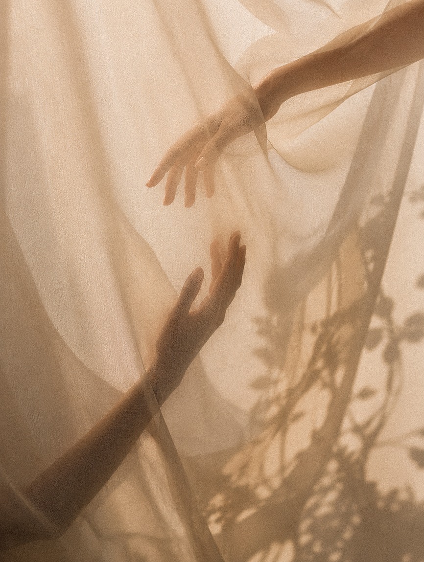Hands reaching through sheer fabric in warm, quiet light